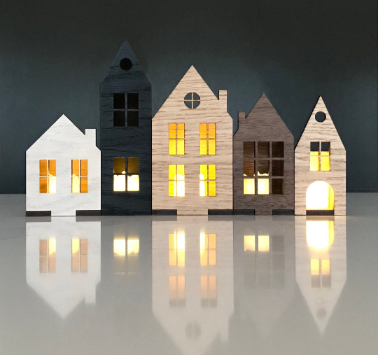 Set of Scaninavian style houses in wood veneer, with battery tea lights glowing in the cut out windows. 